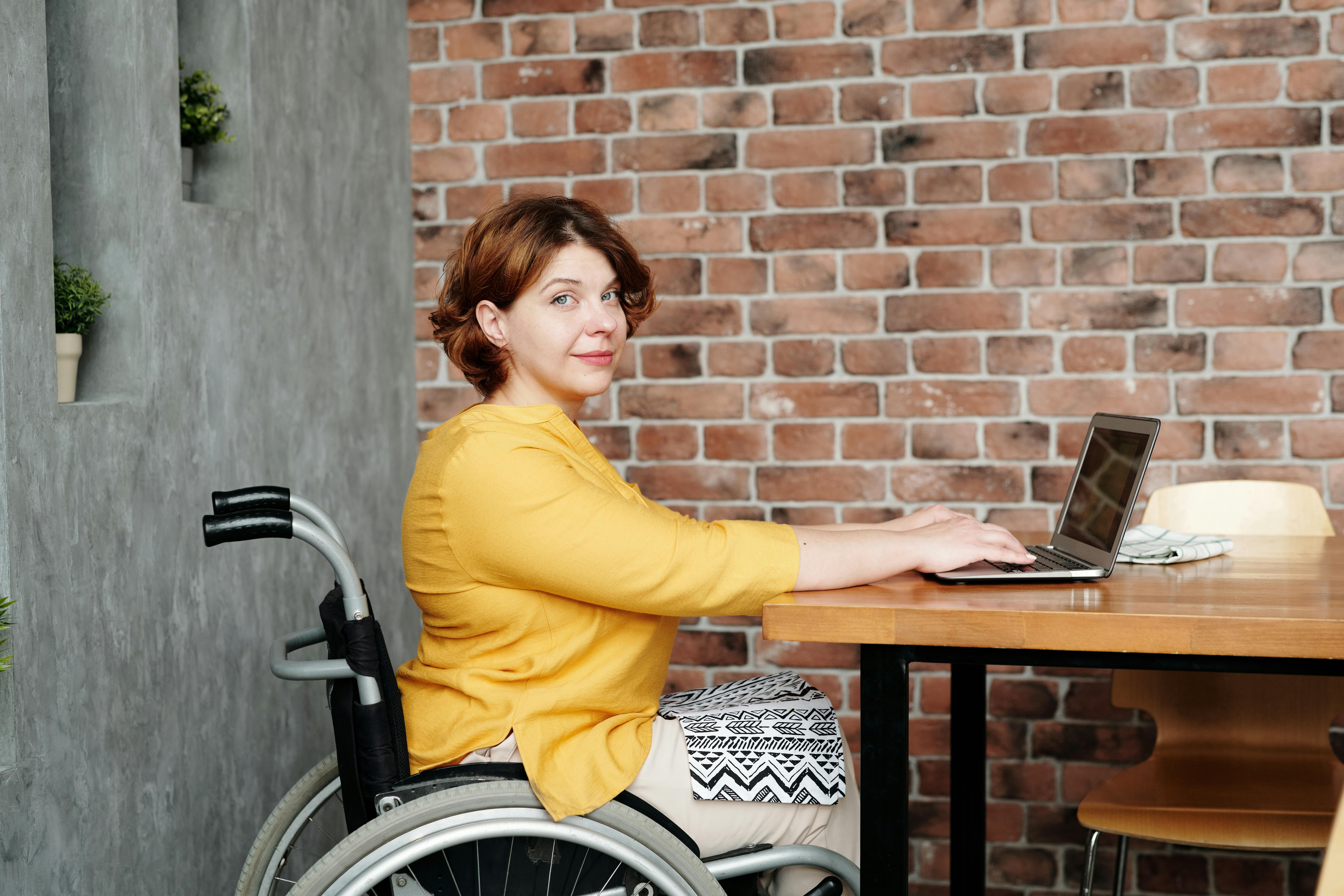 Woman using a wheelchair working on a laptop at a desk for ABility Centre in Adelaide